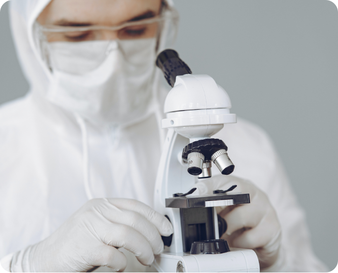 A person in white lab coat looking through microscope.