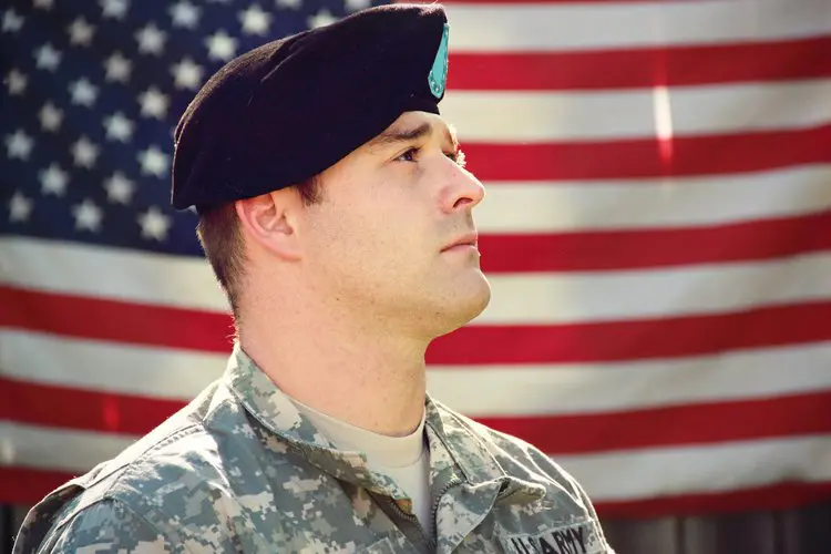 A soldier in fatigues and a hat is looking up.